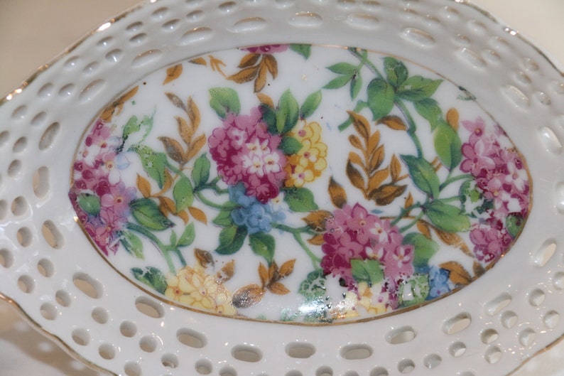 K&ouml;nnte beinhalten: Eine wei&szlig;e Porzellanschale mit einem Blumendesign. Die Schale hat einen gewellten Rand und ein spitzendes Muster um den Rand. Das Blumendesign zeigt rosa, gelbe und blaue Blumen auf wei&szlig;em Hintergrund.