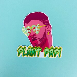 May include: A sticker featuring a cartoon illustration of a person with pink skin, a beard, and green and yellow sunglasses. The text "PLANT PAPI" is written in green and yellow letters with flames on either side.