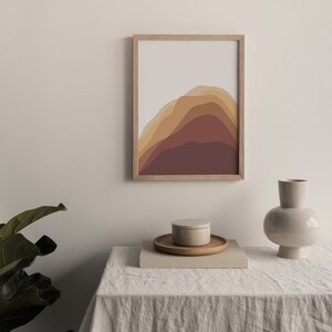 Puede incluir: Una impresi&oacute;n art&iacute;stica abstracta enmarcada con un dise&ntilde;o de monta&ntilde;a en capas en tonos marrones y beige. Una peque&ntilde;a bandeja de madera con un recipiente redondo y un jarr&oacute;n decorativo est&aacute;n sobre una mesa cubierta de lino.