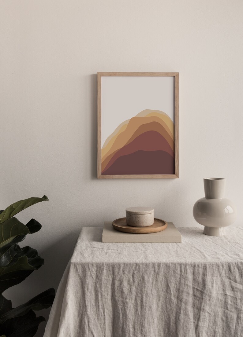 Puede incluir: Una impresi&oacute;n art&iacute;stica abstracta enmarcada con un dise&ntilde;o de monta&ntilde;a en capas en tonos marrones y beige. Una peque&ntilde;a bandeja de madera con un recipiente redondo y un jarr&oacute;n decorativo est&aacute;n sobre una mesa cubierta de lino.