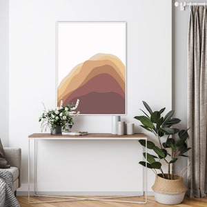 Puede incluir: Una impresi&oacute;n art&iacute;stica abstracta enmarcada con formas en capas en tonos marrones y naranjas. La obra de arte cuelga sobre una consola de madera con un marco de metal blanco. Una planta en maceta y flores a&ntilde;aden un toque natural a la habitaci&oacute;n.