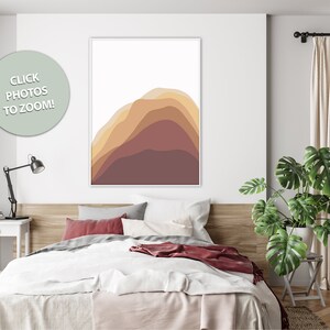 Puede incluir: Una impresi&oacute;n art&iacute;stica abstracta enmarcada con formas en capas en tonos marr&oacute;n, beige y burdeos. La obra de arte cuelga sobre una cama con ropa de cama blanca, almohadas rojas y un cabecero de madera. Una planta verde est&aacute; cerca de la ventana.