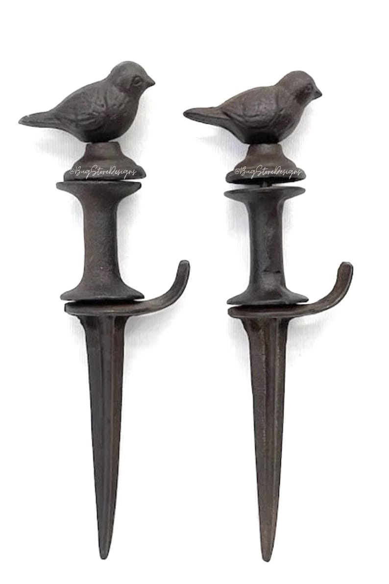 May include: Two dark brown metal garden stakes, each topped with a bird figurine. The stakes have a hook and a pointed end for easy ground insertion. The birds are perched atop a decorative base.