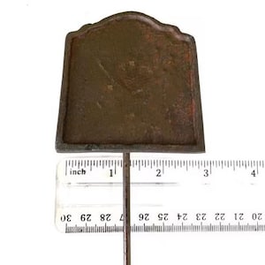 May include: A weathered, brown metal garden marker with a decorative top. The marker is approximately 7.6 cm tall and is attached to a thin metal rod. The background is white.
