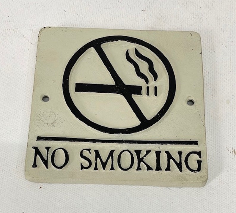 May include: White cast iron sign with a black no smoking symbol and the text "NO SMOKING".
