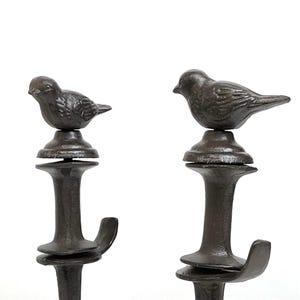 May include: Two dark brown metal hooks with a bird perched on top. The hooks have a decorative design and are suitable for hanging items. The birds are detailed and add a touch of nature to the design.
