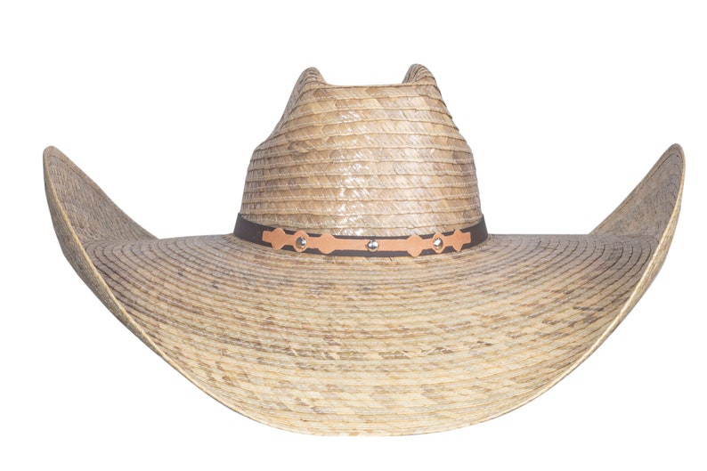 K&ouml;nnte beinhalten: Ein breitkrempiger Strohhut im Cowboy-Stil mit einem braunen Lederband und dekorativen Metallverzierungen. Der Hut hat eine hellbraune Farbe und eine leicht spitze Krone.