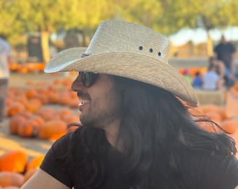 May include: A light beige straw cowboy hat with a pinched crown and a wide, curved brim. The hat features a dark braided band around the base of the crown and three small, circular black ventilation eyelets on each side of the crown.