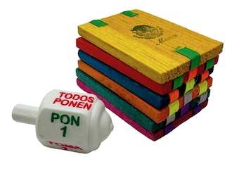 May include: A white wooden spinning top with the words "TODOS PONEN" and "PON 1" in red and green. The top is next to a stack of colorful wooden blocks with a green, red, blue, orange, pink, green, gray, and purple stripe.