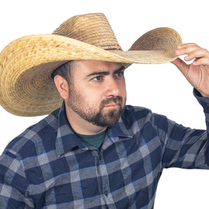 K&ouml;nnte beinhalten: Ein Mann tr&auml;gt einen breitkrempigen Strohhut im Cowboy-Stil und ein blau-graues kariertes Hemd.