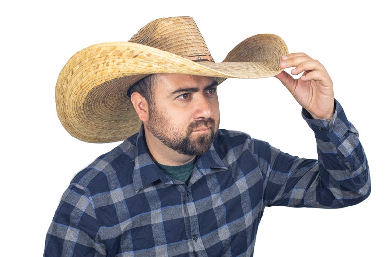 K&ouml;nnte beinhalten: Ein Mann tr&auml;gt einen breitkrempigen Strohhut im Cowboy-Stil und ein blau-graues kariertes Hemd.
