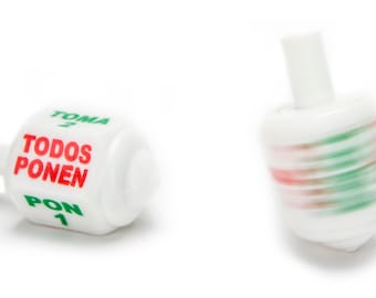 May include: White plastic spinning top with red and green stripes. The top has the words "TOMA 2" and "PON 1" in green and "TODOS PONEN" in red.