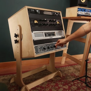 Op de afbeelding: Een 10U 16-inch diepe fader rack gemaakt van natuurlijk lichtgekleurd hout. Het rack heeft een schuin ontwerp met verstelbare zijknoppen en bevat meerdere zwarte en zilveren audioapparatuur met knoppen, schijven en het QSC-logo.