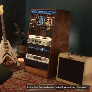 Op de afbeelding: Een 24U schuin houten rack met een chocoladekleurige afwerking, voorzien van een geventileerde bovenkant en rubberen voetjes. Het rack is gevuld met diverse audioapparatuurmodules, waaronder een Cloudlifter-unit en een QSC-versterker in een stevig frame.