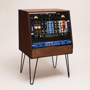 Op de afbeelding: Een audio-apparatuurrek van donker hout met vier zwarte metalen haarspeldpoten. Het rek bevat meerdere rack-units, waaronder een Radial Workhorse, een Effectron II en diverse knoppen, schakelaars en analoge VU-meters op de voorpanelen.