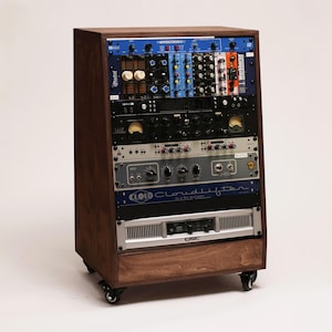 Op de afbeelding: Een houten studio rack-behuizing op wielen met diverse audioapparatuurmodules. Het rack bevat meerdere eenheden, waaronder een blauwe Effectron, een zwarte Apollo-interface, een Cloudlifter CL-1 en een zilverkleurige QSC-versterker.