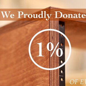 May include: A close-up of a wooden rack with a white circle that says "1%" and the text "We Proudly Donate" above it and "Of Every Sale" below it. The text "Studio Carpenter Gear" is in a circle in the top left corner of the image.