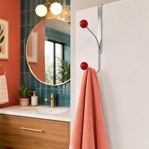 May include: A silver over-the-door hook featuring two prongs with glossy red spherical ends. The metal hook is mounted on the top edge of a white door and holds a single coral-colored towel draped over the lower prong, leaving the top prong empty.