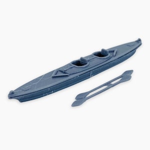 May include: A blue kayak with two seats and a pair of paddles. The kayak is a small model, likely a toy or decorative item. The paddles are positioned next to the kayak, ready for use.