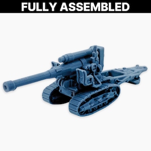 Puede incluir: Un cañón de artillería en miniatura azul grisáceo completamente ensamblado, con un cañón largo y orugas de tanque. El texto "FULLY ASSEMBLED" se muestra encima del cañón. El cañón es un modelo detallado, probablemente para juegos de mesa o exhibición.