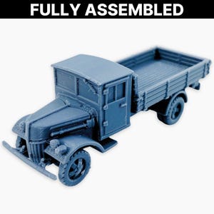 Może przedstawiać: W pełni zmontowany, niebieski model ciężarówki z platformą. Ciężarówka ma szczegółową kabinę z drzwiami i oknami, przednim zderzakiem i szczegółową kratką. Tekst "FULLY ASSEMBLED" znajduje się u góry obrazu.