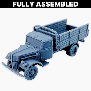 Może przedstawiać: W pełni zmontowana, niebiesko-szara zabawka ciężarówka o szczegółowym designie. Ciężarówka posiada kabinę, skrzynię ładunkową z bocznymi szynami i cztery koła. Tekst "FULLY ASSEMBLED" jest wyświetlany nad ciężarówką.