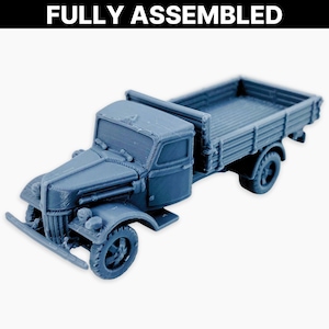 Może przedstawiać: W pełni zmontowana, szaro-niebieska ciężarówka zabawka o szczegółowym designie. Ciężarówka posiada kabinę, platformę i cztery koła. Tekst "FULLY ASSEMBLED" jest wyświetlany nad ciężarówką.