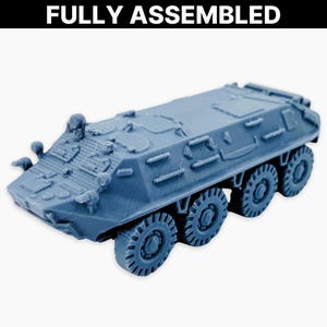 Op de afbeelding: Een volledig geassembleerd, blauwgrijs model van een gepantserde personeelsdrager. Het voertuig heeft acht wielen en diverse gedetailleerde kenmerken. De tekst "FULLY ASSEMBLED" staat bovenaan de afbeelding.