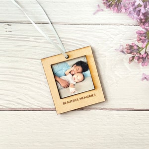 May include: A wooden photo frame with a light brown finish, featuring a photo of a mother and child. The frame has a white ribbon attached to the top and the text "BEAUTIFUL MEMORIES" is engraved below the photo.