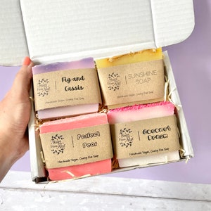 Può includere: Una scatola regalo piena di quattro saponette vegane artigianali e cruelty-free. Le saponette sono etichettate "Fico e Cassis", "Sapone Sole", "Pera Perfetta" e "Sogno di Cocco".