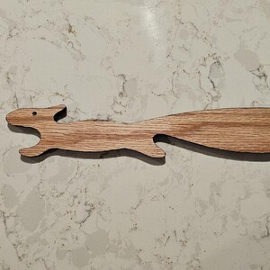 May include: A wooden squirrel-shaped keychain with a black cord. The squirrel is carved in a light brown wood and has a simple design.