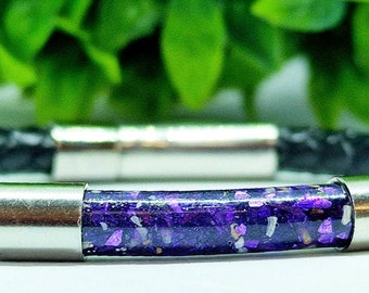 Può includere: Un braccialetto in pelle nera con un tubo riempito di glitter viola e accenti in metallo argentato.
