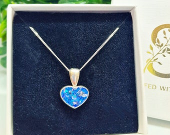 Può includere: Una collana d'argento con un ciondolo a forma di cuore riempito di glitter blu. La collana è esposta in una scatola bianca con un rivestimento in velluto nero.