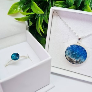 May include: A set of jewellery featuring a silver ring with a blue and green stone and a silver necklace with a pendant featuring a blue and white resin design.