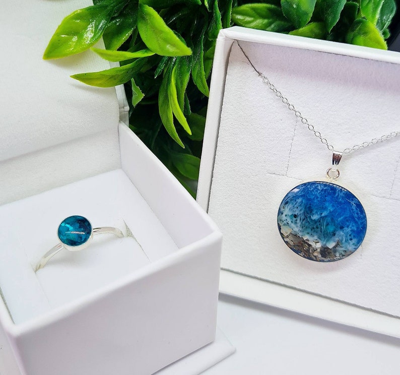 May include: A set of jewellery featuring a silver ring with a blue and green stone and a silver necklace with a pendant featuring a blue and white resin design.