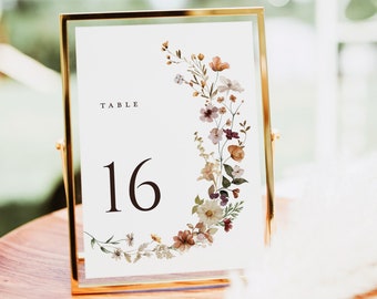 May include: A gold-framed table number card with a white background and a floral design. The card says "TABLE 16" and features a watercolour illustration of a wreath of flowers in shades of pink, orange, and brown.