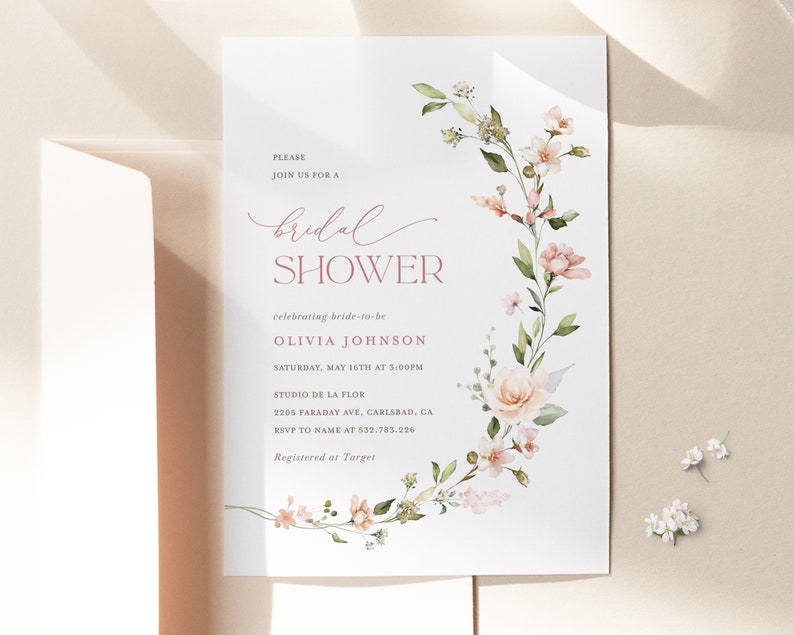 May include: A white bridal shower invitation with pink floral illustrations. The text reads "Please join us for a bridal shower celebrating bride-to-be Olivia Johnson, Saturday, May 16th at 3:00PM, Studio de la Flor, 2205 Faraday Ave, Carlsbad, CA, RSVP to name at 532.783.226, Registered at Target."