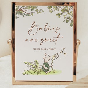 May include: A white sign with a gold frame and a green leafy border. The sign says "Babies are sweet" and "Please take a treat". There is a cartoon piglet holding a dandelion with seeds blowing in the wind.