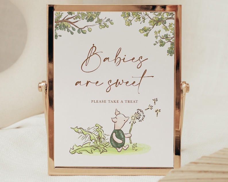 May include: A white sign with a gold frame and a green leafy border. The sign says "Babies are sweet" and "Please take a treat". There is a cartoon piglet holding a dandelion with seeds blowing in the wind.