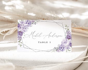 Puede incluir: Una tarjeta de lugar rectangular con un diseño floral. La tarjeta presenta el nombre "Michel Anderson" y "TABLE 1" en escritura elegante. Rosas lavanda y vegetación enmarcan un borde geométrico plateado.