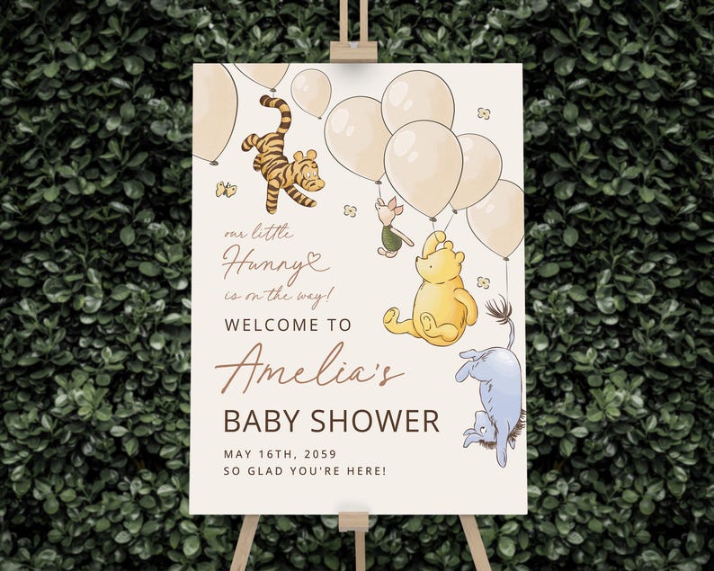 Pode incluir: Uma placa de boas-vindas para ch&aacute; de beb&ecirc; com personagens de Winnie the Pooh e bal&otilde;es. A placa inclui o texto "our little Hunny is on the way!" e "Welcome to Amelia's Baby Shower, May 16th, 2059". A placa est&aacute; em um cavalete de madeira.