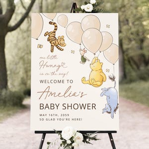 Pode incluir: Placa de boas-vindas para ch&aacute; de beb&ecirc; com personagens do Ursinho Pooh, bal&otilde;es e o texto "Our little Hunny is on the way!" e "Welcome to Amelia's Baby Shower". A placa est&aacute; em um cavalete.