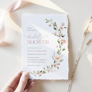May include: A white bridal shower invitation with a floral design in shades of pink and green. The text reads "Please join us for a bridal shower celebrating bride-to-be Olivia Johnson Saturday, May 16th at 3:00PM Studio de la Flor 2205 Faraday Ave, Carlsbad, CA RSVP to name at 532-783-226 Registered at Target"