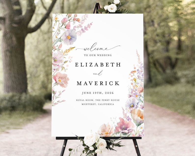 May include: A white wedding welcome sign with a floral design featuring pink, purple, and yellow flowers. The sign reads "Welcome to our wedding, Elizabeth and Maverick, June 19th, 2026, Royal Room, The Perry House, Monterey, California."