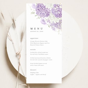 May include: A white menu card with a floral design featuring purple and white hydrangeas. The menu lists appetizers, entrées, and dessert options for August 25, 2059. The menu is on a white plate with dried grass.