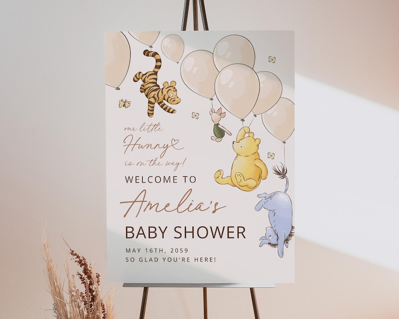 Pode incluir: Uma placa de ch&aacute; de beb&ecirc; com ilustra&ccedil;&otilde;es de personagens de Winnie the Pooh e bal&otilde;es. A placa diz "Bem-vindo ao ch&aacute; de beb&ecirc; de Amelia" com a data de 16 de maio de 2059. A placa est&aacute; em um cavalete.