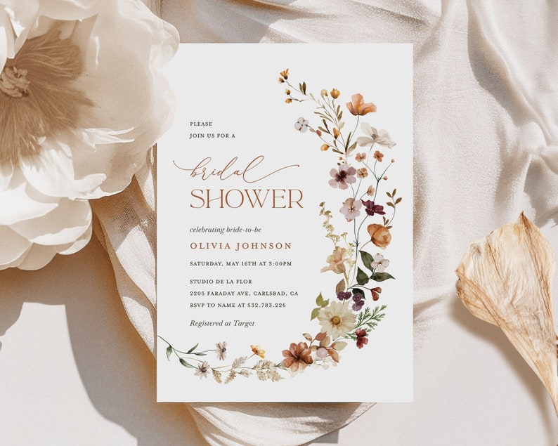 May include: A floral bridal shower invitation with a wreath of watercolor flowers in shades of pink, orange, and yellow. The text reads "Please join us for a bridal shower celebrating bride-to-be Olivia Johnson Saturday, May 16th at 3:00PM Studio de la Flor 2205 Faraday Ave, Carlsbad, CA RSVP to name at 532.783.226 Registered at Target"