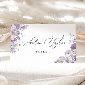 May include: Purple floral wedding table card with the name "Aiden Taylor" and the text "Table 1".