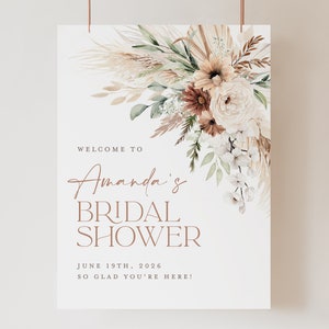 Op de afbeelding: Een bruidsdouchebord met een bloemstuk in neutrale tinten. Het bord leest "Welcome to Amanda's Bridal Shower" met de datum 19 juni 2026 en de zin "So glad you're here!"