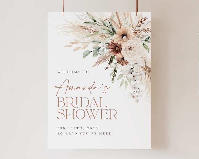 Op de afbeelding: Een bruidsdouchebord met een bloemstuk in neutrale tinten. Het bord leest "Welcome to Amanda's Bridal Shower" met de datum 19 juni 2026 en de zin "So glad you're here!"